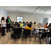 A room full of people sitting at a table listening to a female presenter.