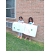 Two little girls posing with their posters in front of a brick wall.