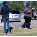 Two women standing in grass near a silver car.